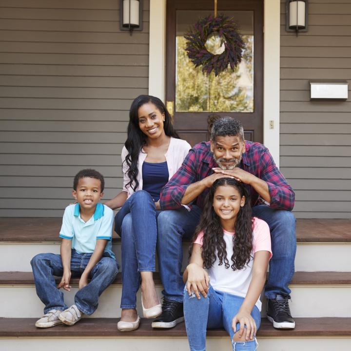 family with children sit on steps of new home